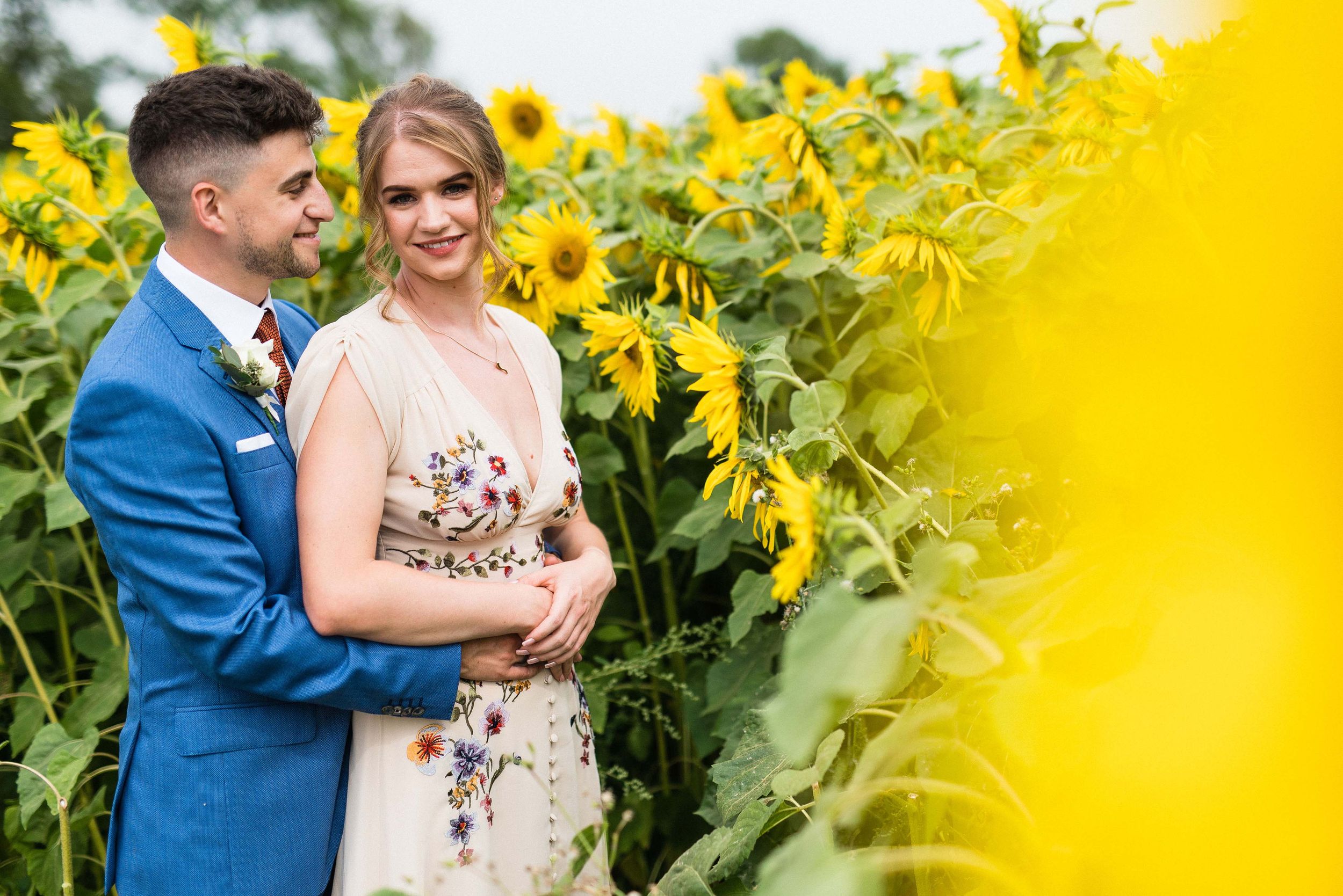 Georgie and Sam in a bright sunflower field at their summer garden wedding