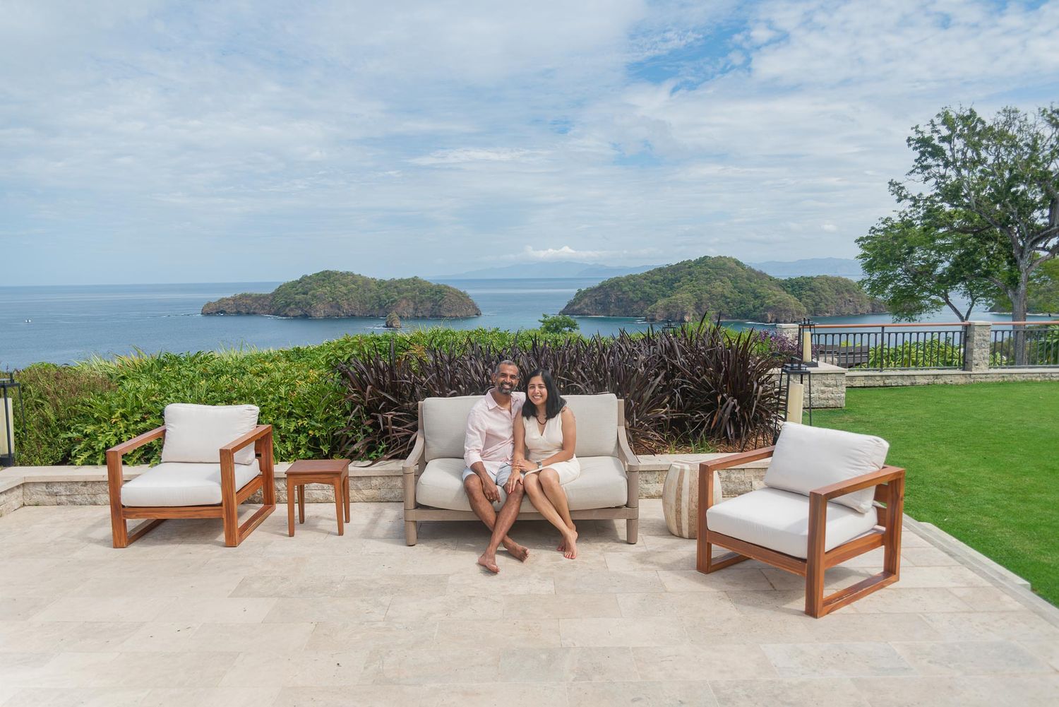 Two women sit on outdoor patio furniture overlooking a scenic ocean view with tropical islands in the background.