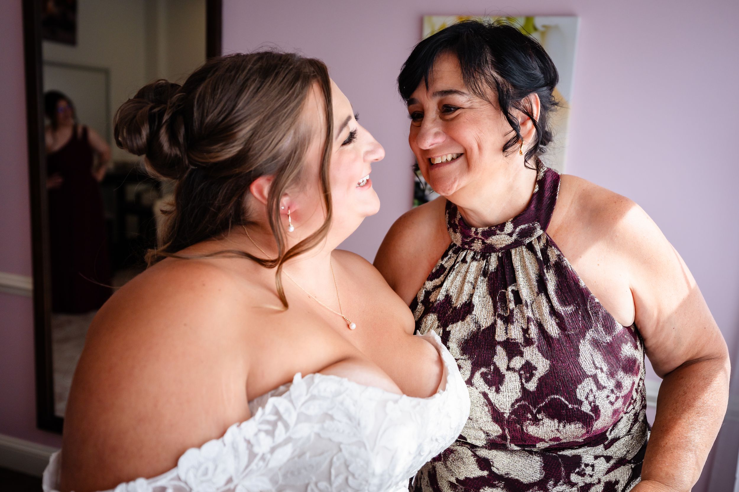 Bride and mother sharing a joyful embrace while smiling at each other during wedding preparations.