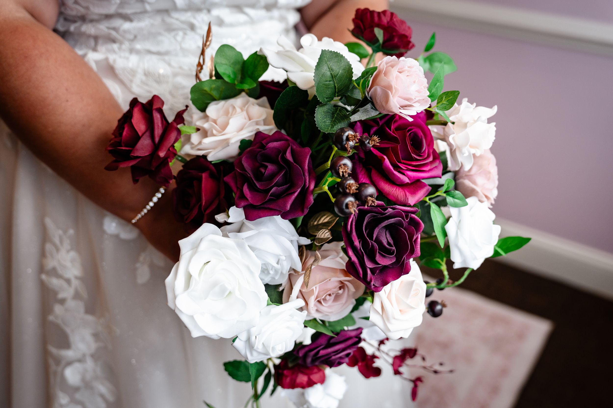 Bride holding a stunning wedding bouquet featuring deep burgundy, blush, and white roses with green foliage.