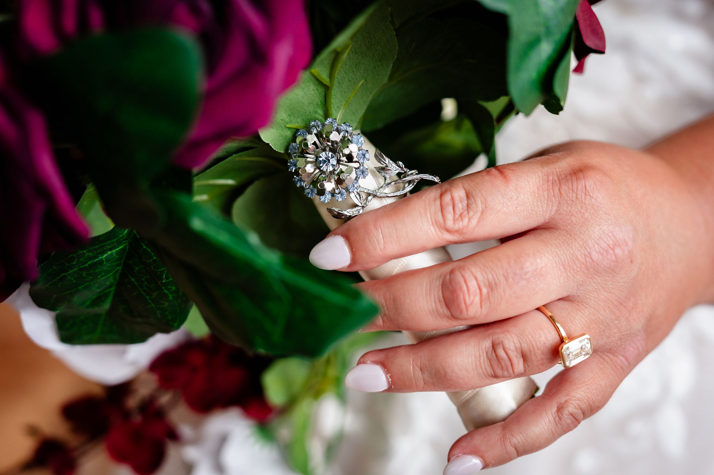 Close-up of bride's diamond engagement ring and gold wedding band with floral bouquet.