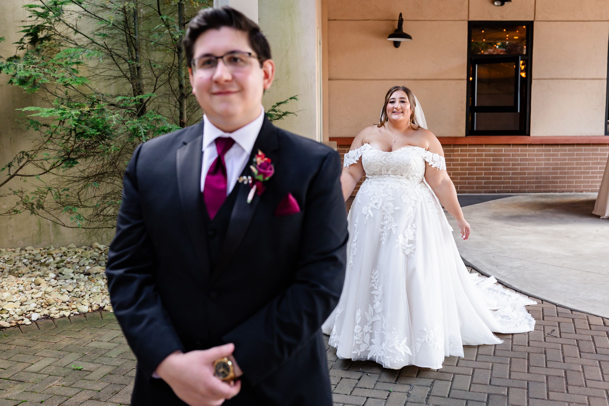 First look moment as bride in lace gown approaches groom outdoors.