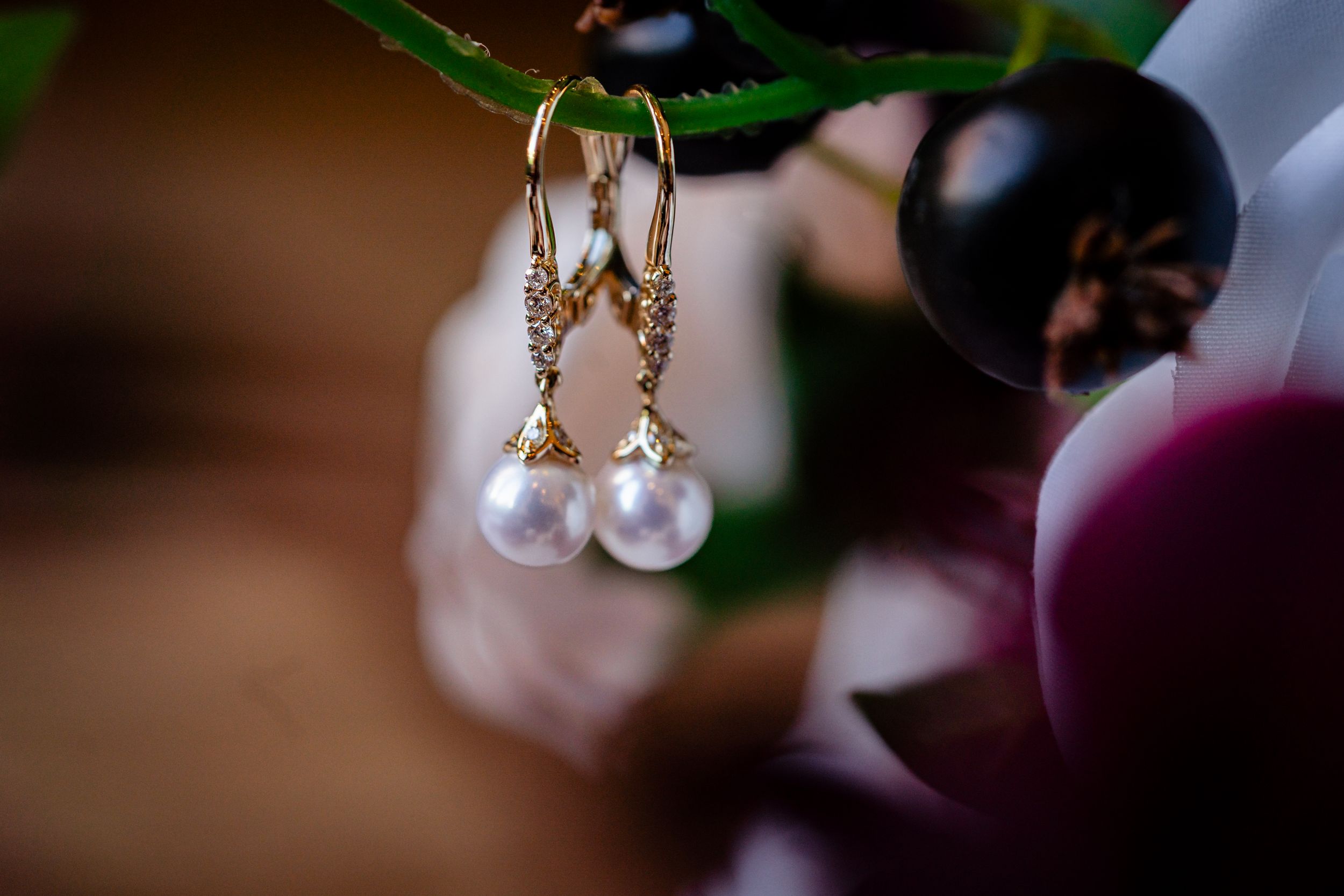 Elegant gold drop earrings with pearl and diamond accents displayed among soft floral blooms.