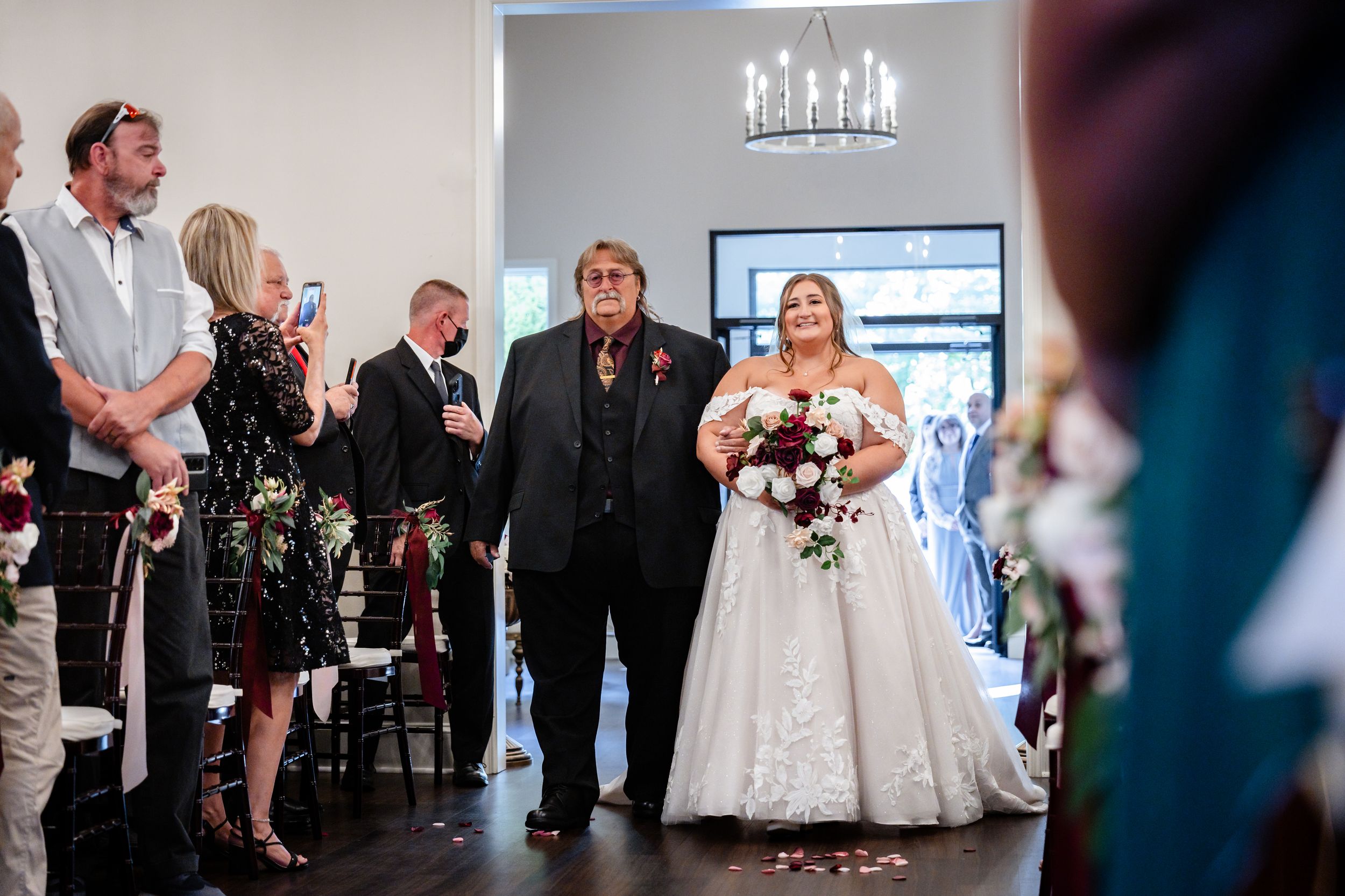 Bride in white ball gown walking down the aisle with escort during wedding ceremony.