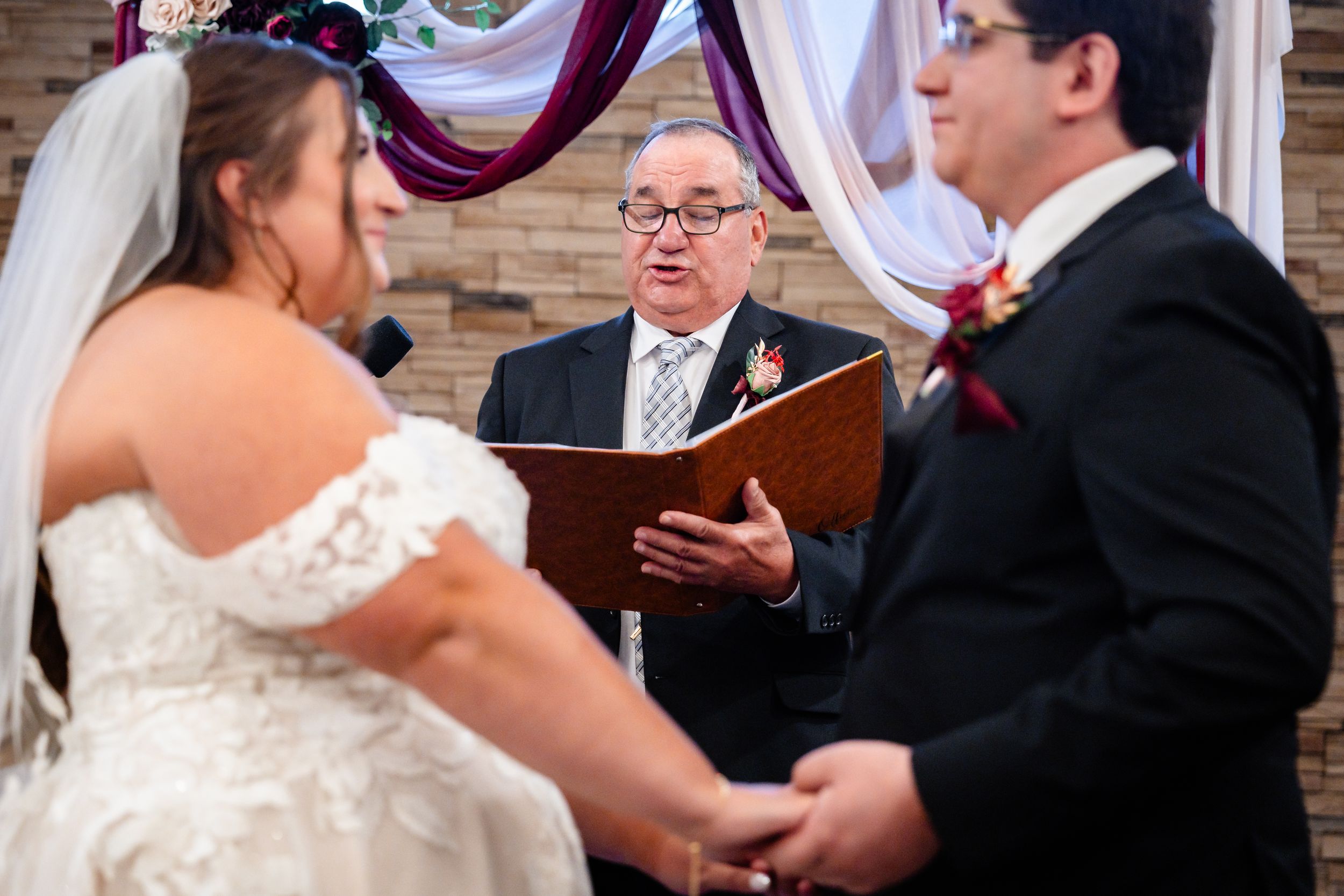 Wedding officiant reading vows to bride and groom during indoor ceremony.