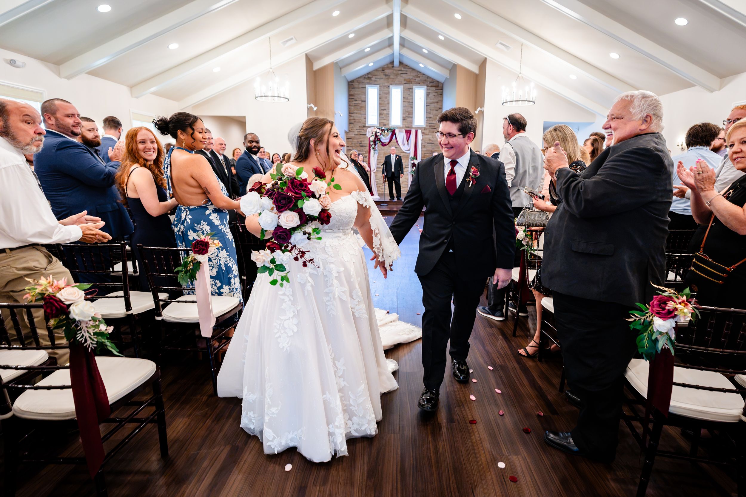Newlyweds joyfully walking back down the aisle hand in hand after wedding ceremony in elegant chapel.