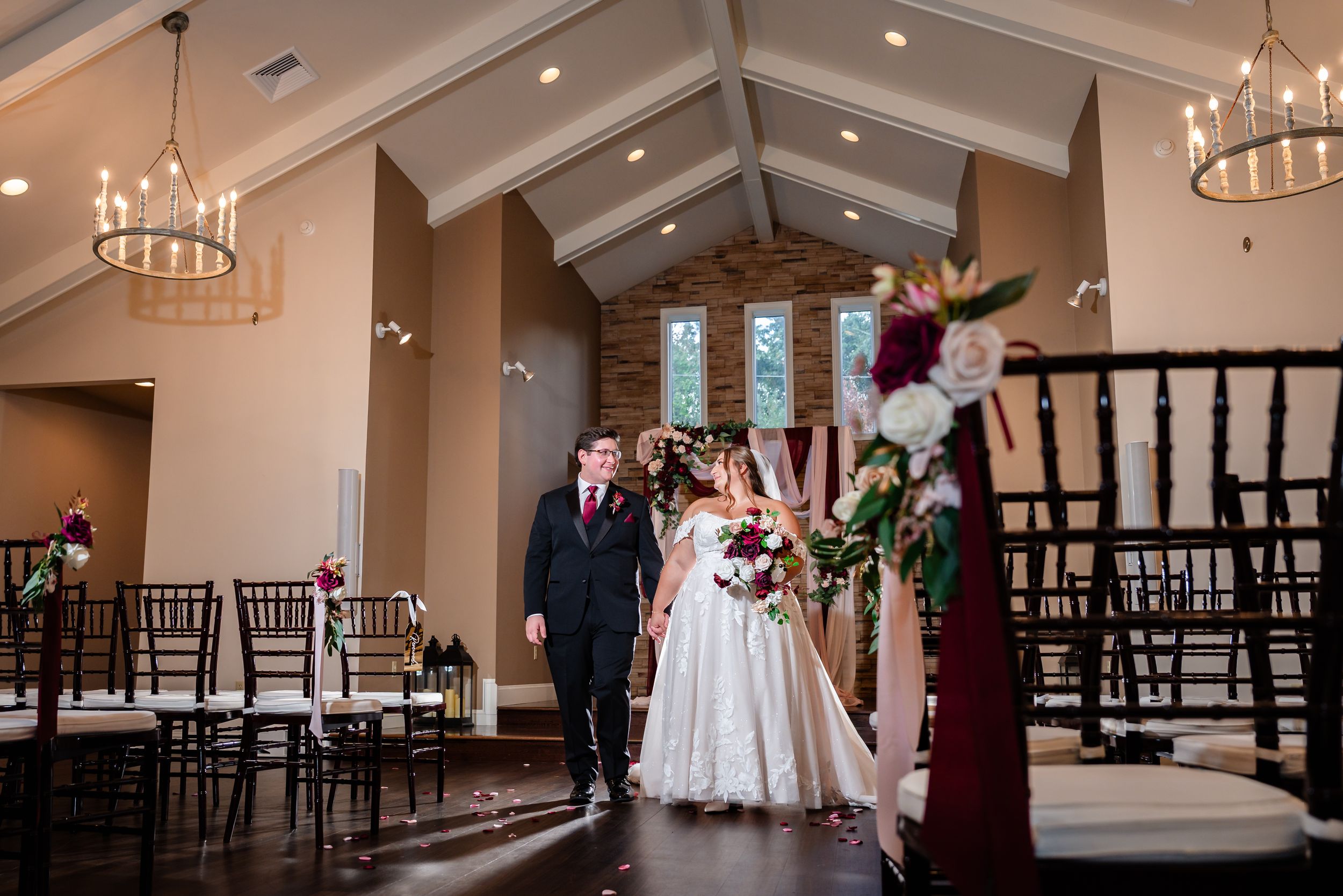 Bride and groom walking down the aisle in a beautiful chapel venue with vaulted ceilings and chandeliers.