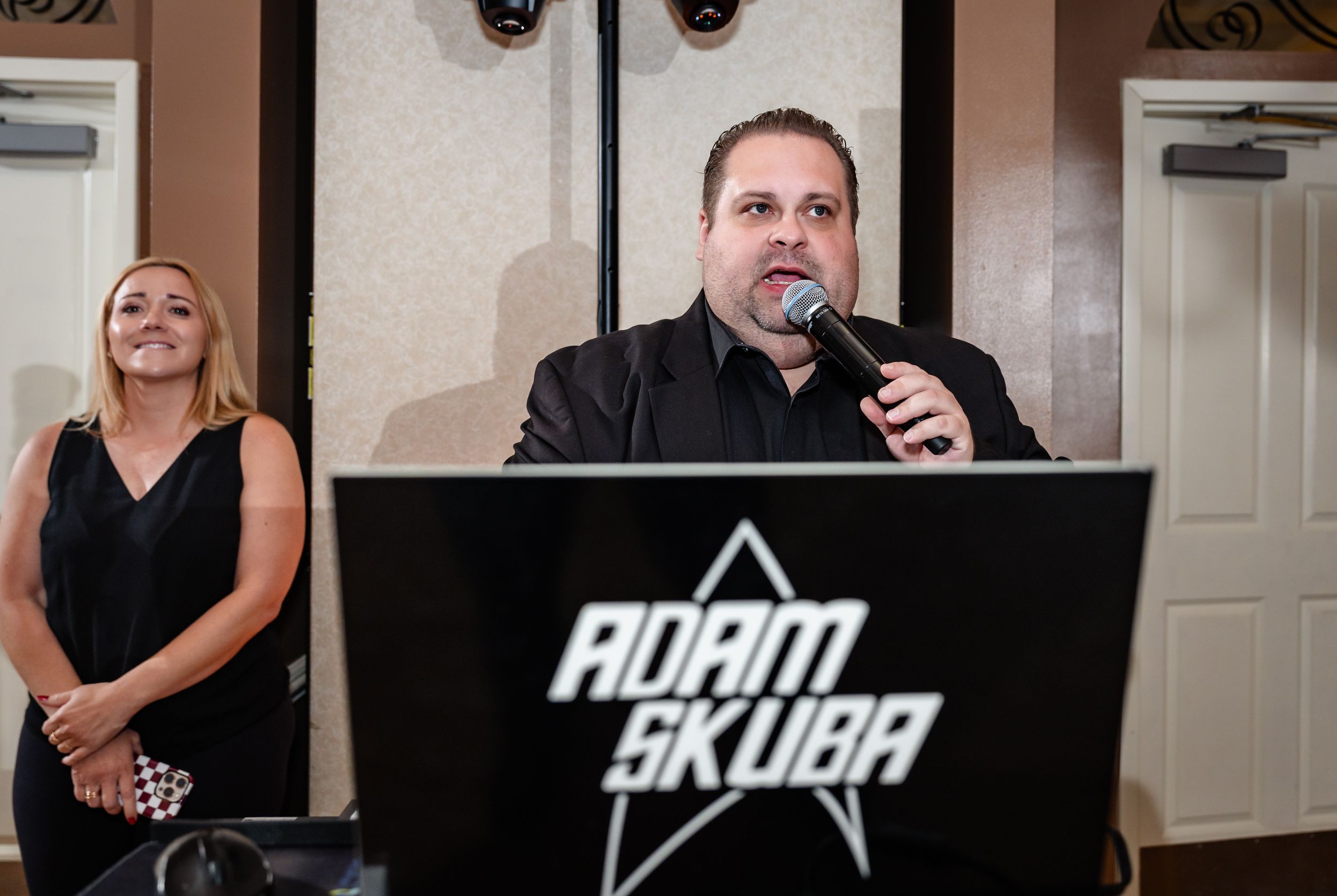 Man speaking at Adam Skuba podium with woman smiling beside him at formal event.