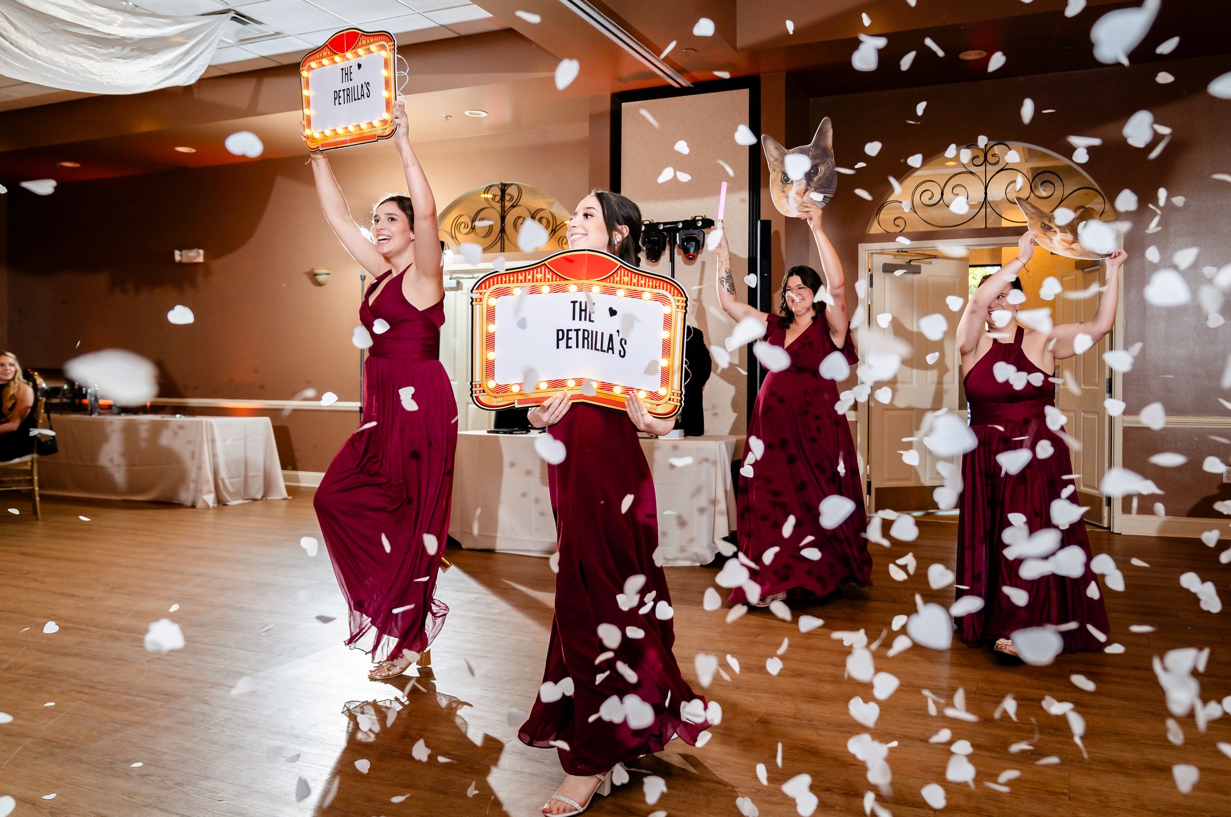 Bridesmaids in burgundy gowns celebrating with confetti shower at wedding reception.