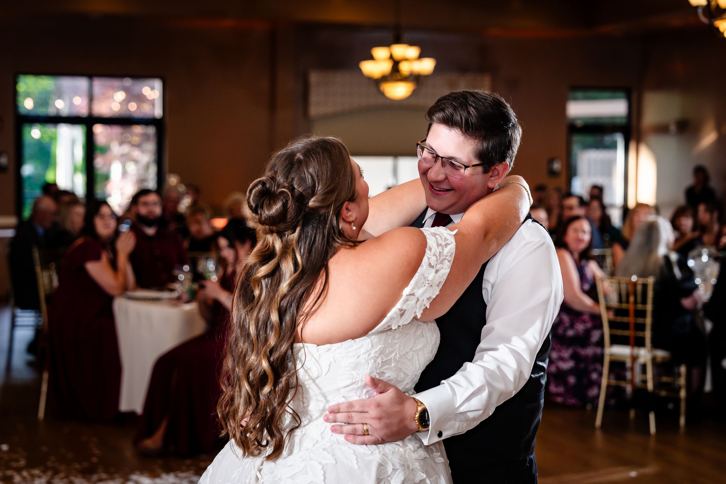 Bride and groom share a joyful first dance embrace, smiling at each other in an elegant wedding reception venue.