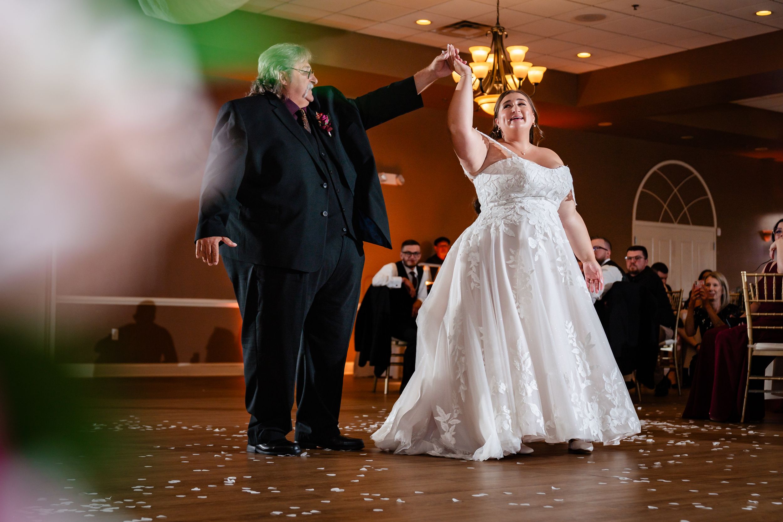 Bride in lace gown sharing a first dance with partner on decorated wedding reception dance floor.