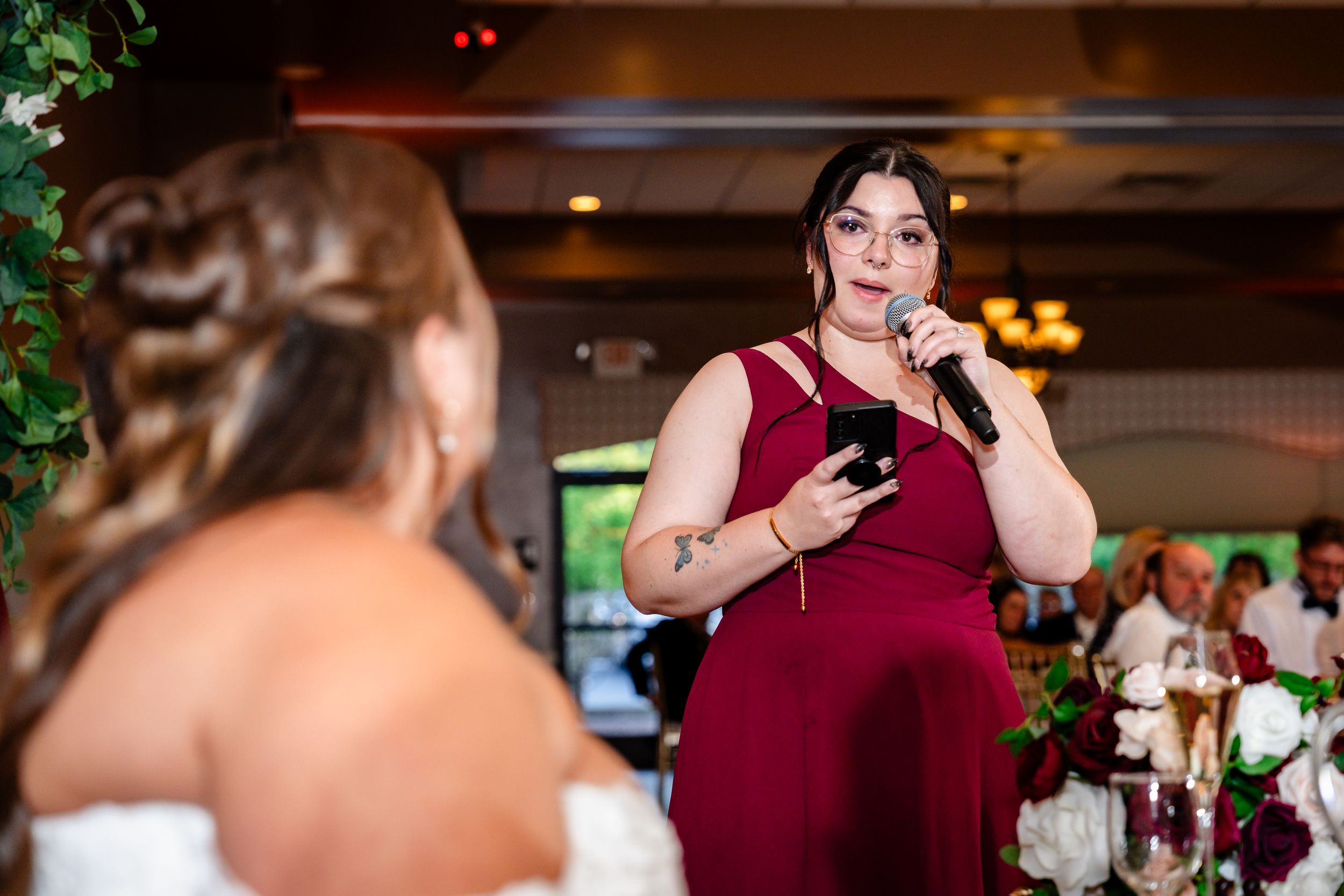 Bridesmaid in red dress giving a heartfelt speech with microphone at an elegant wedding reception.