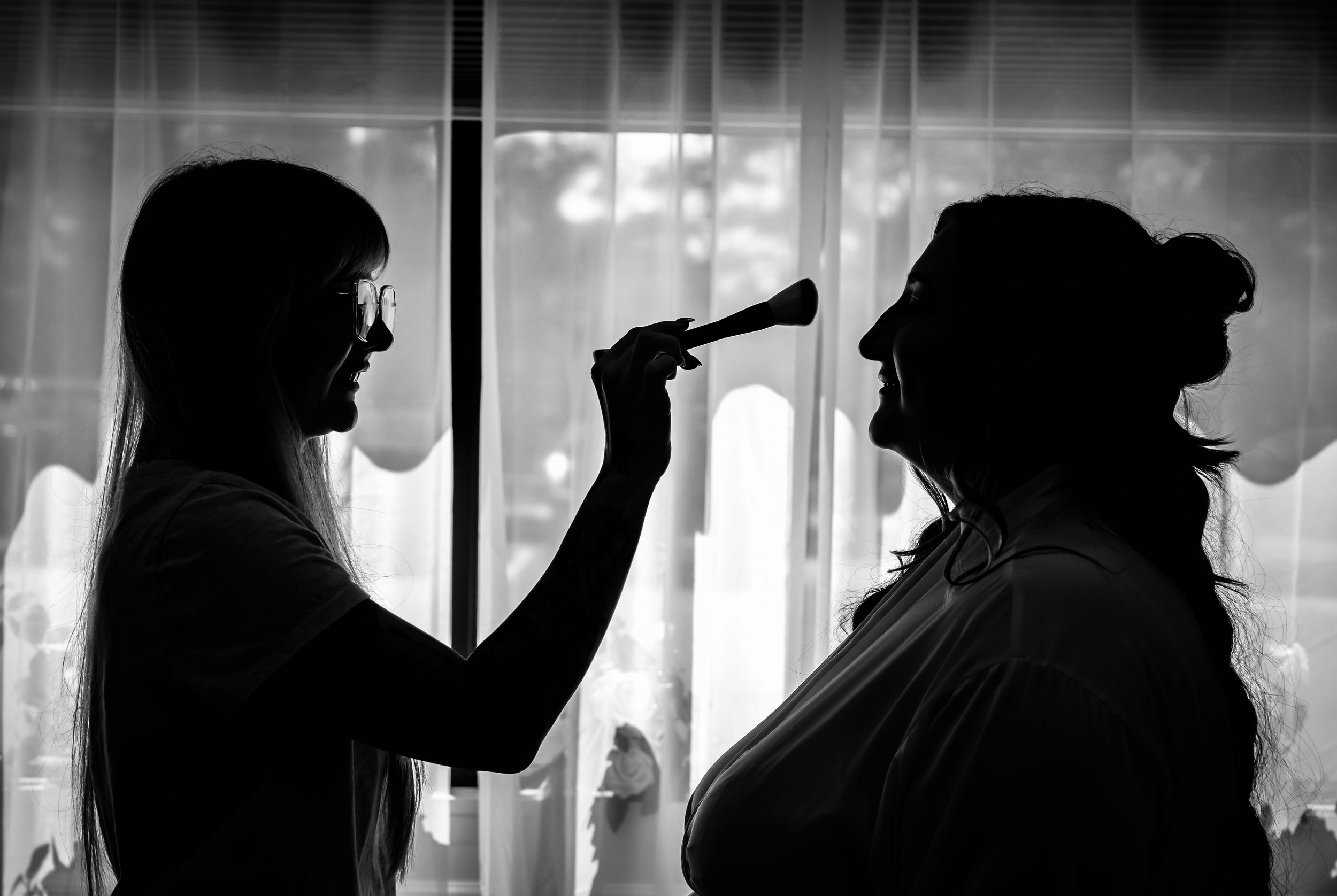 Black and white silhouette of makeup artist applying makeup to bride before wedding ceremony.