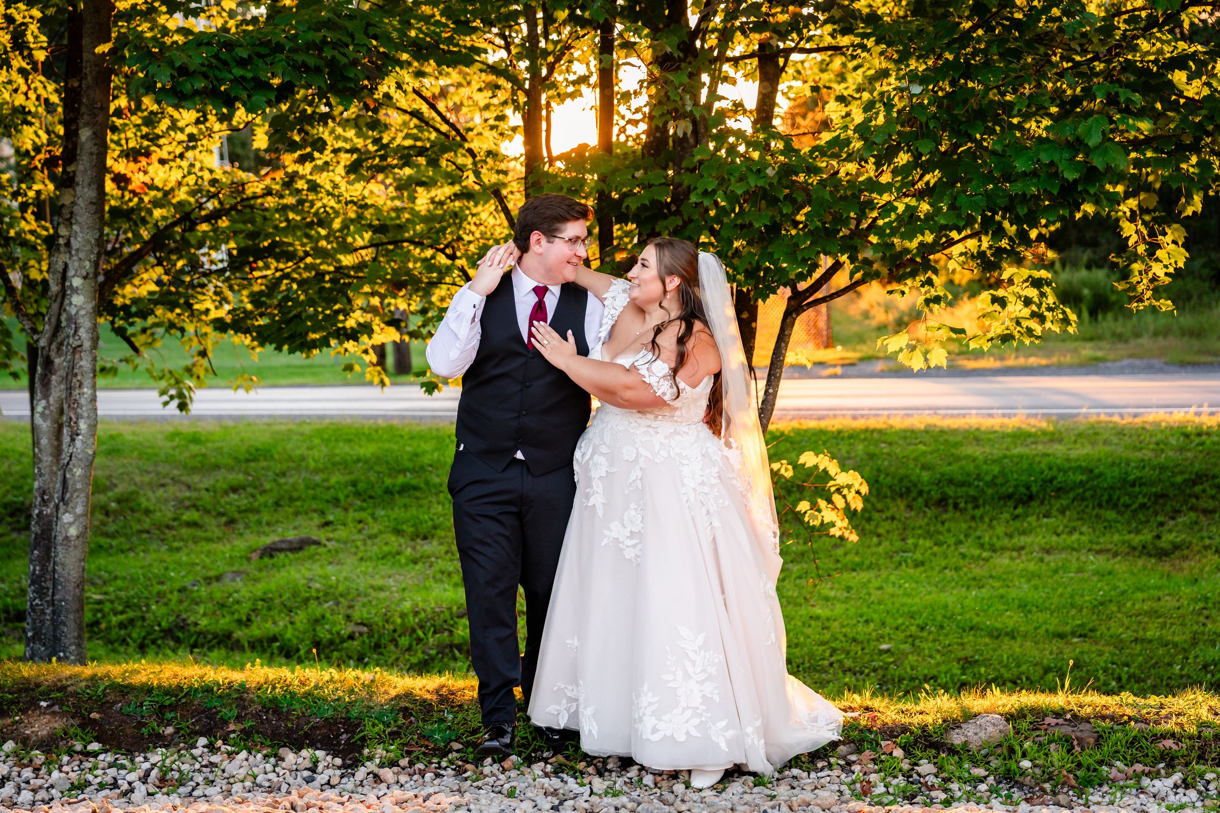 Bride and groom share a romantic dance outdoors at golden hour surrounded by lush green trees.
