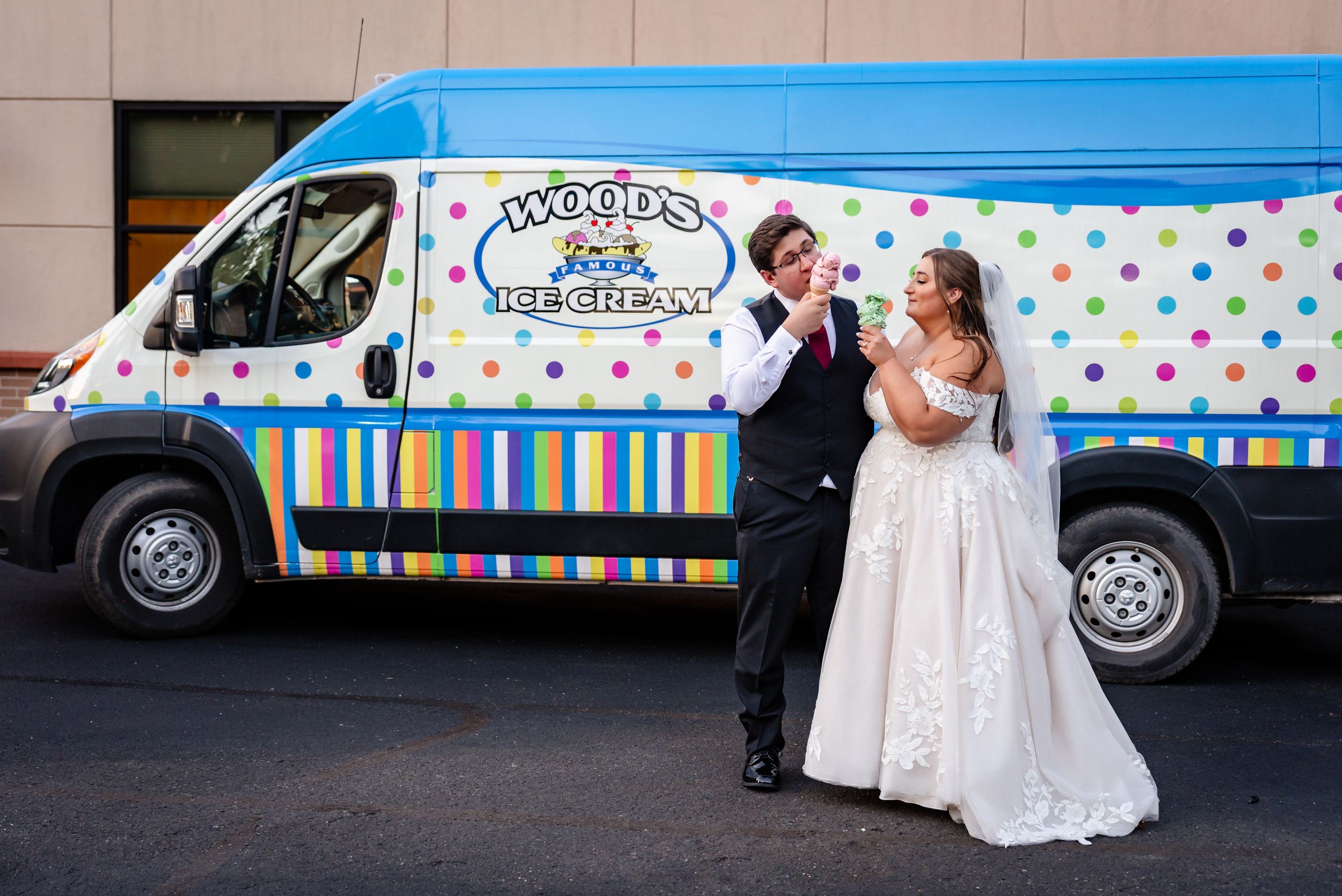 Joyful bride and groom sharing ice cream in front of a colorful Woods Ice Cream van.