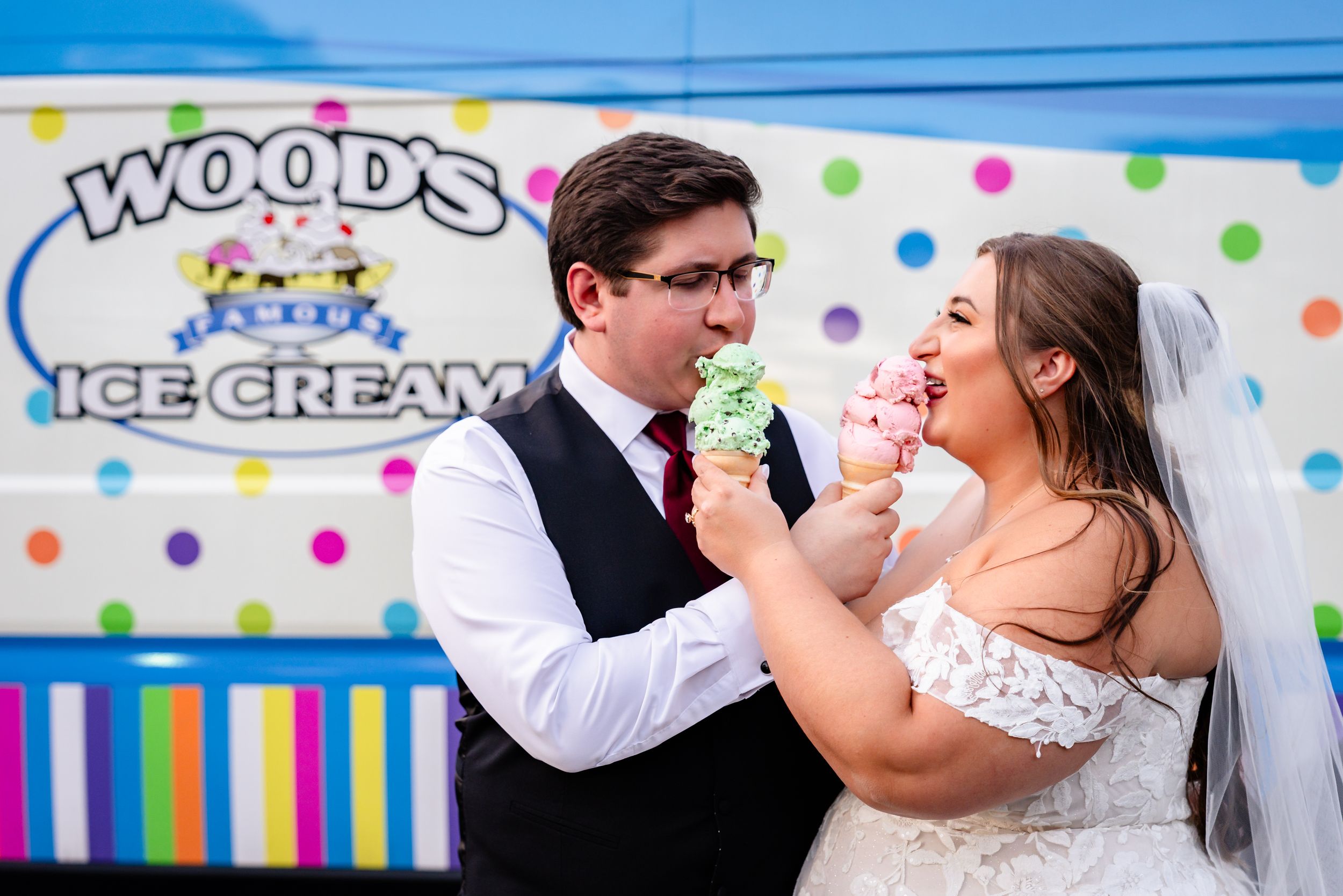 Bride and groom playfully share ice cream cones at Woods Ice Cream truck on their wedding day.