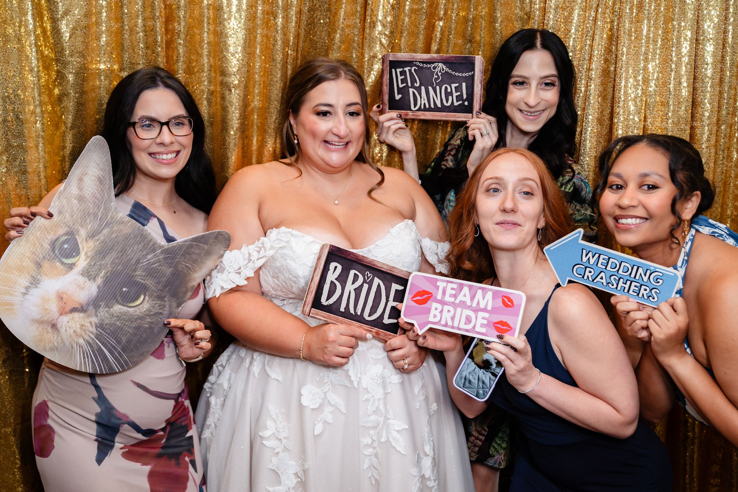 Bride poses with friends in photo booth holding fun signs including Bride and Team Bride at wedding.