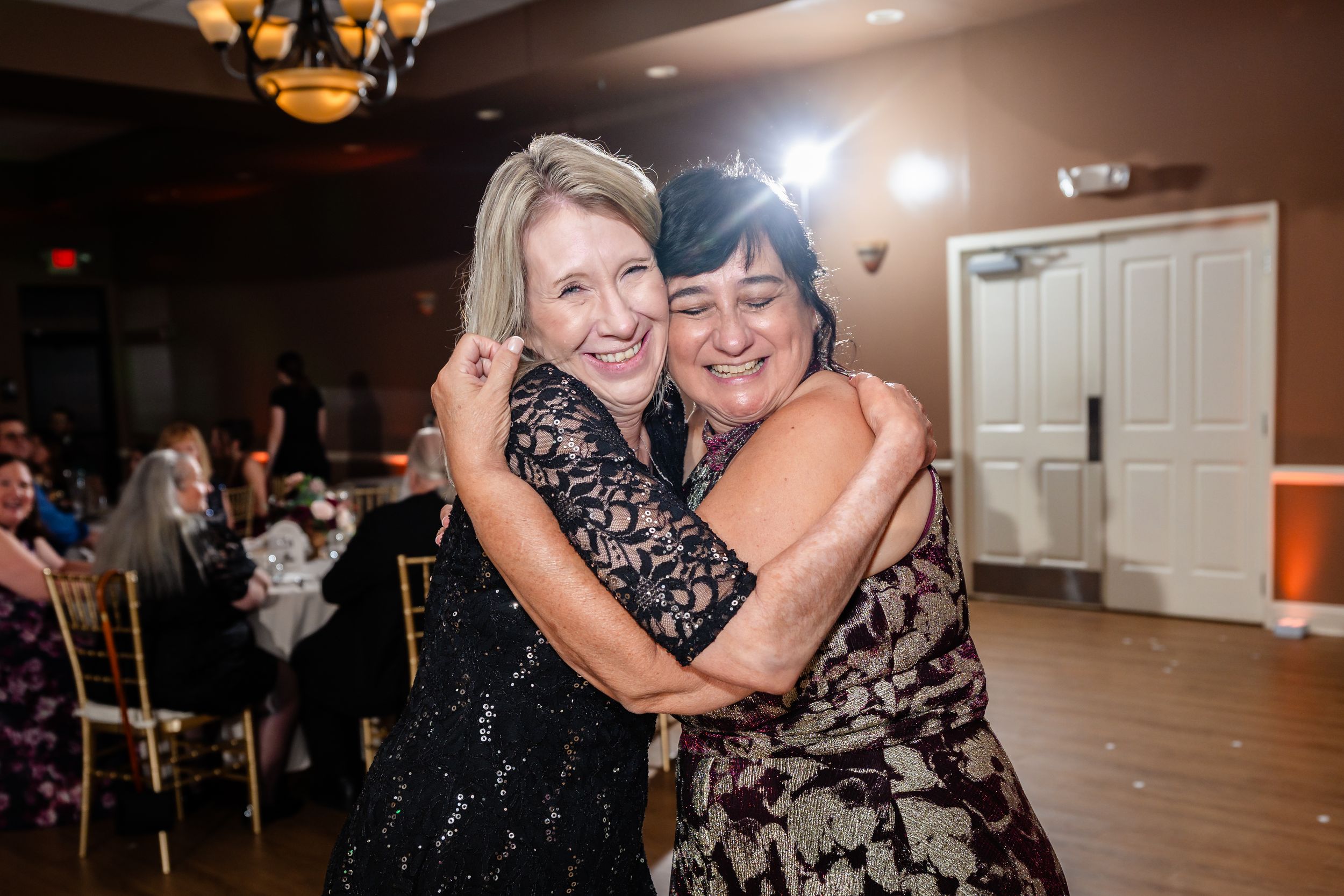 Two women share a warm embrace and smile together on the wedding reception dance floor.