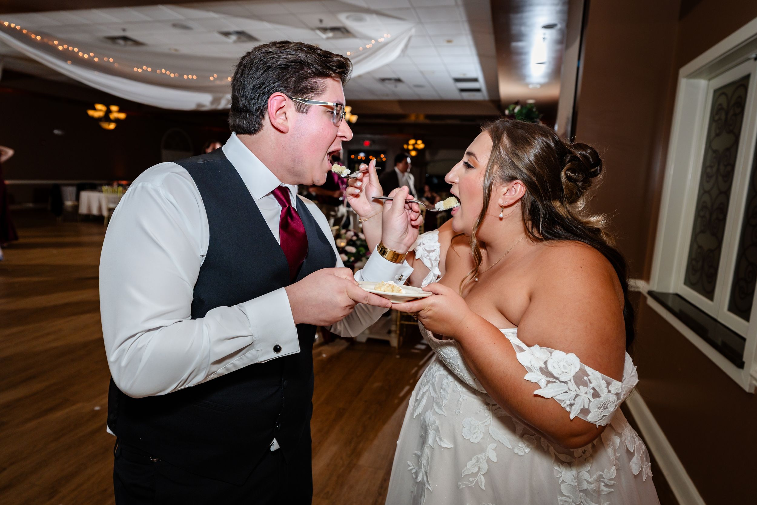Bride and groom playfully feeding each other wedding cake at their reception celebration.