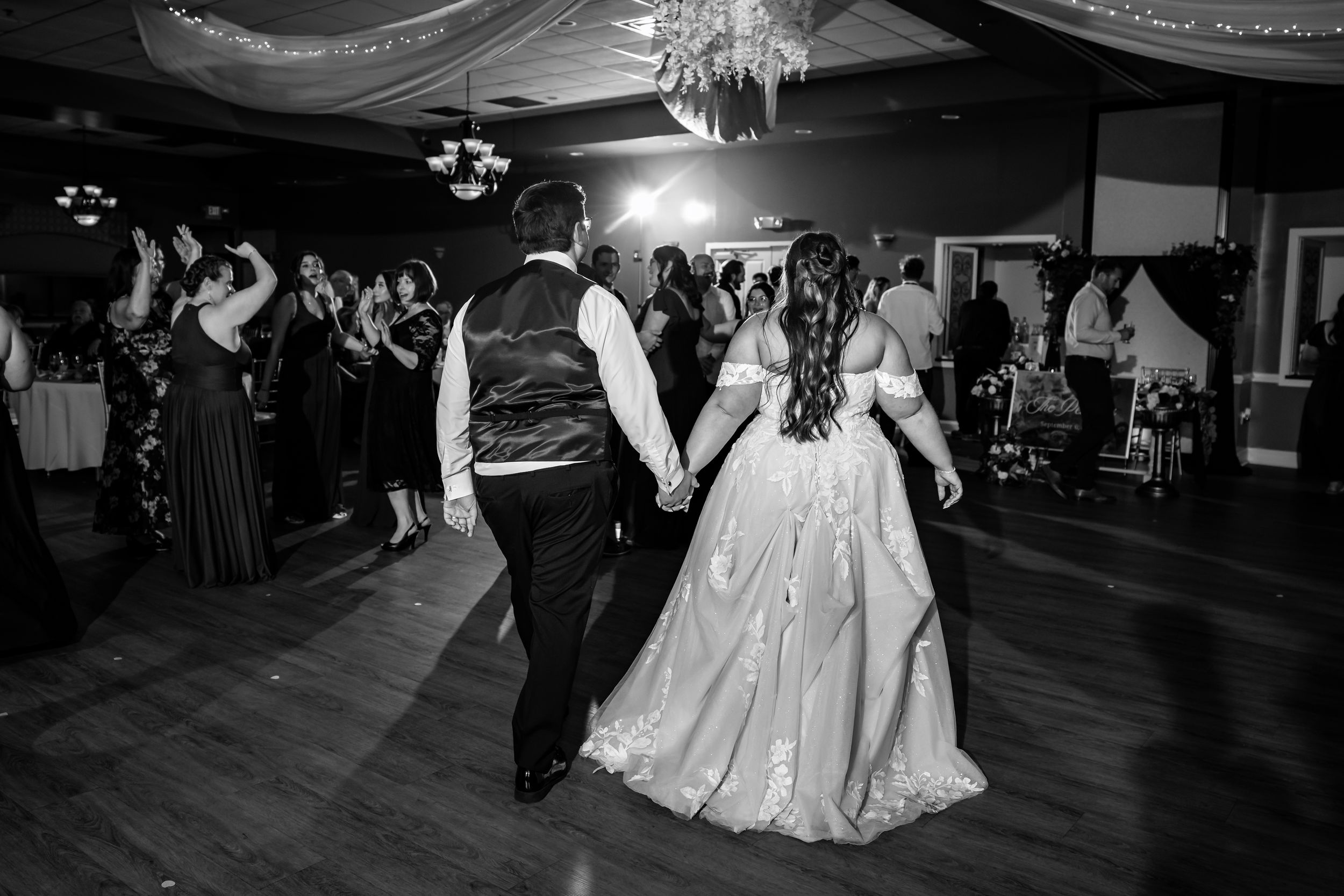 Bride and groom holding hands on the dance floor surrounded by guests at their wedding reception.