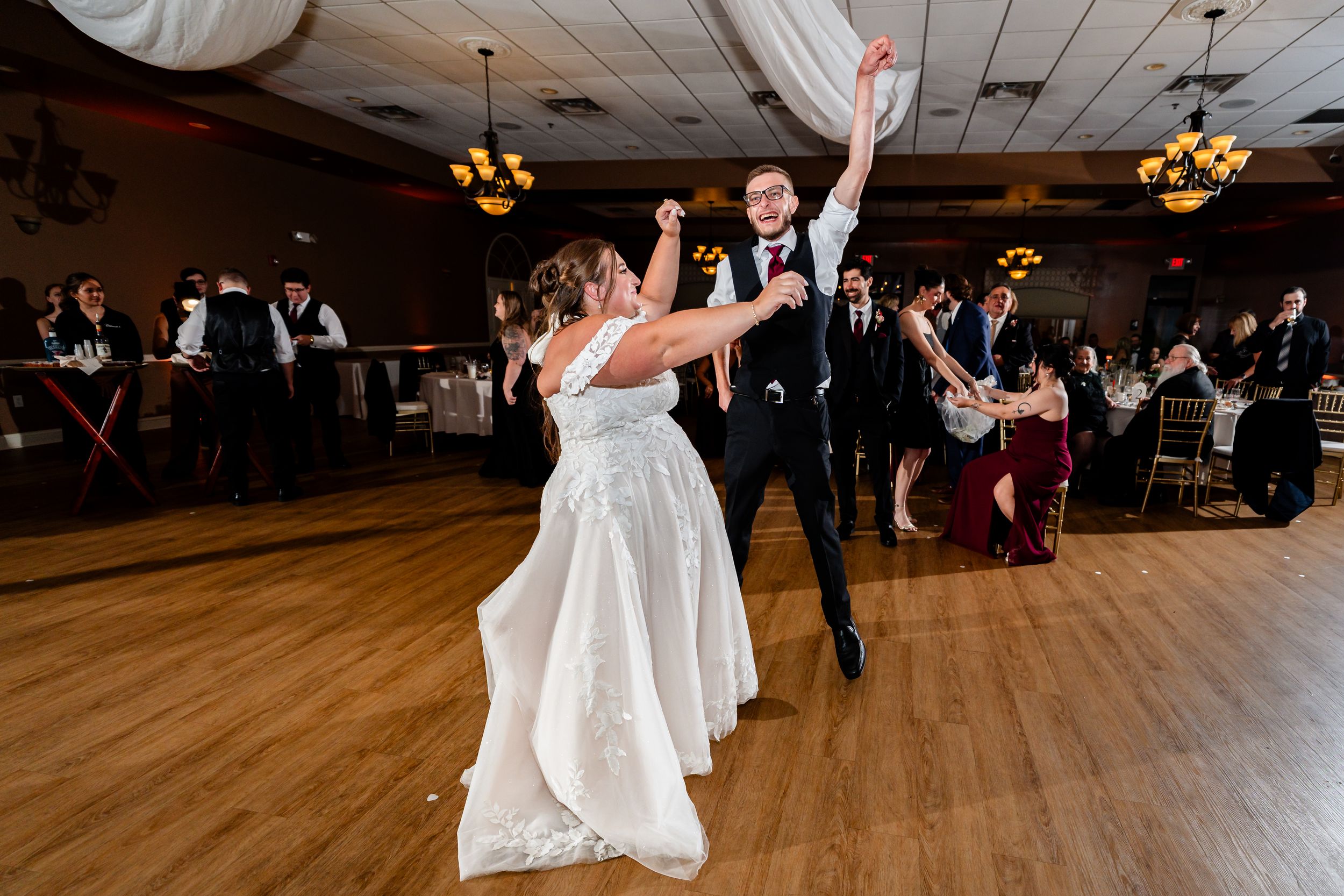 Bride and groom share joyful first dance on wooden ballroom floor at wedding reception.