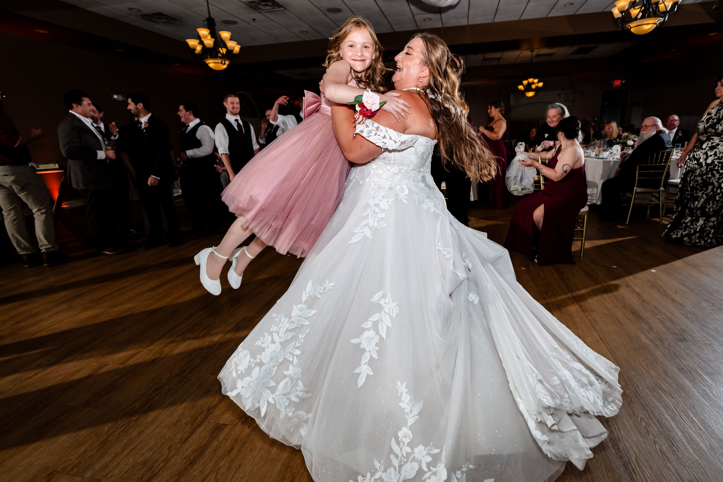 Bride twirls a young flower girl in a pink dress on the wedding reception dance floor.