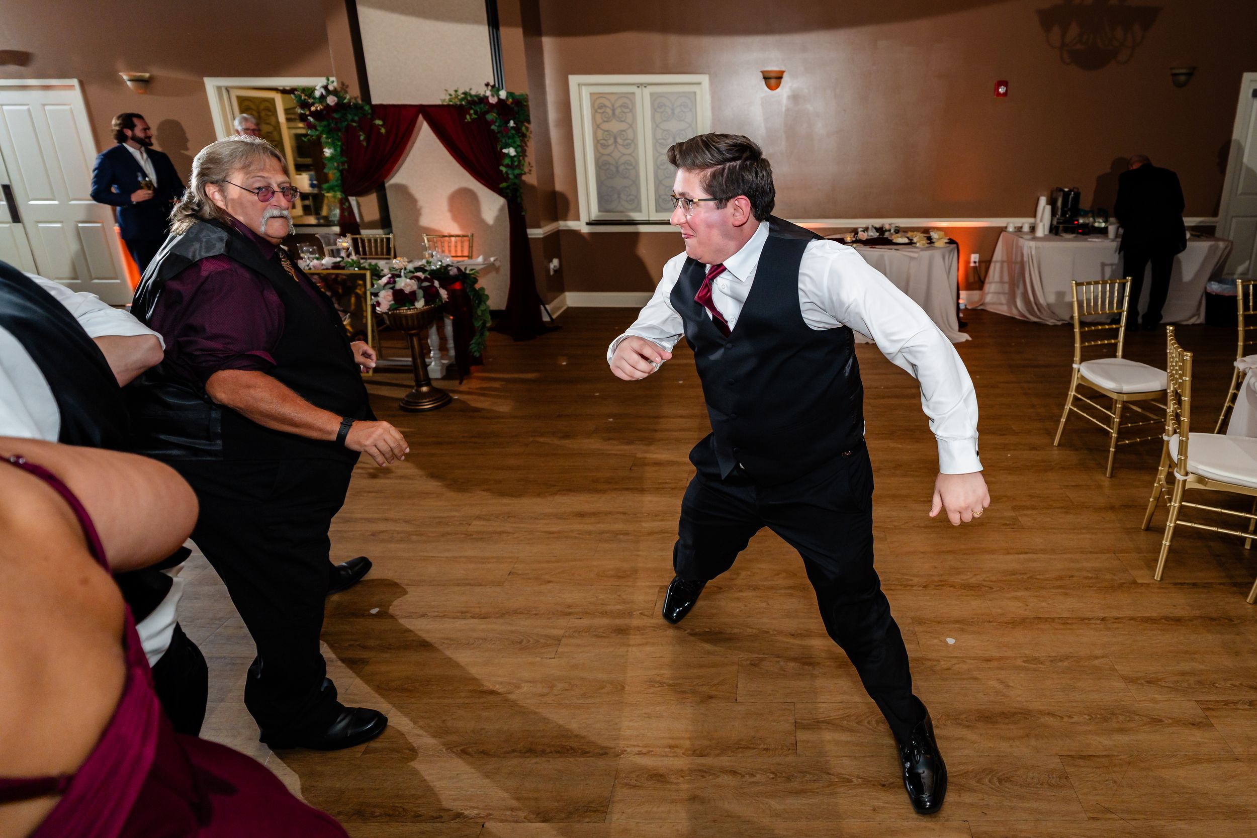 Energetic wedding reception dancer in black vest and white shirt performing on the dance floor.