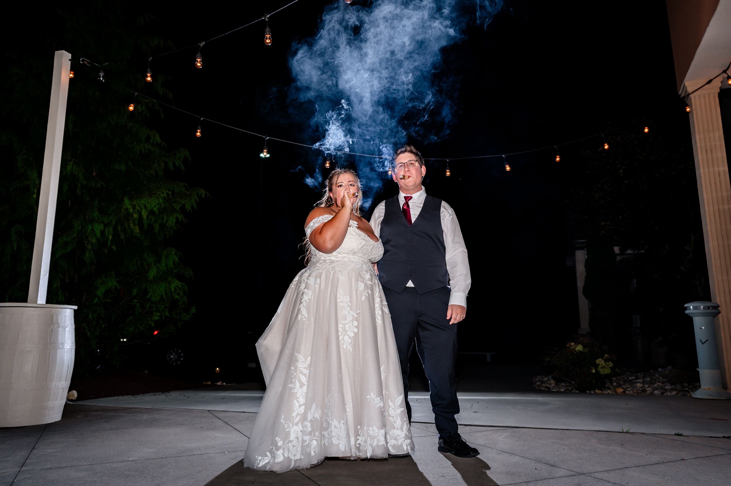 Bride and groom pose together outdoors at night under string lights after wedding ceremony.