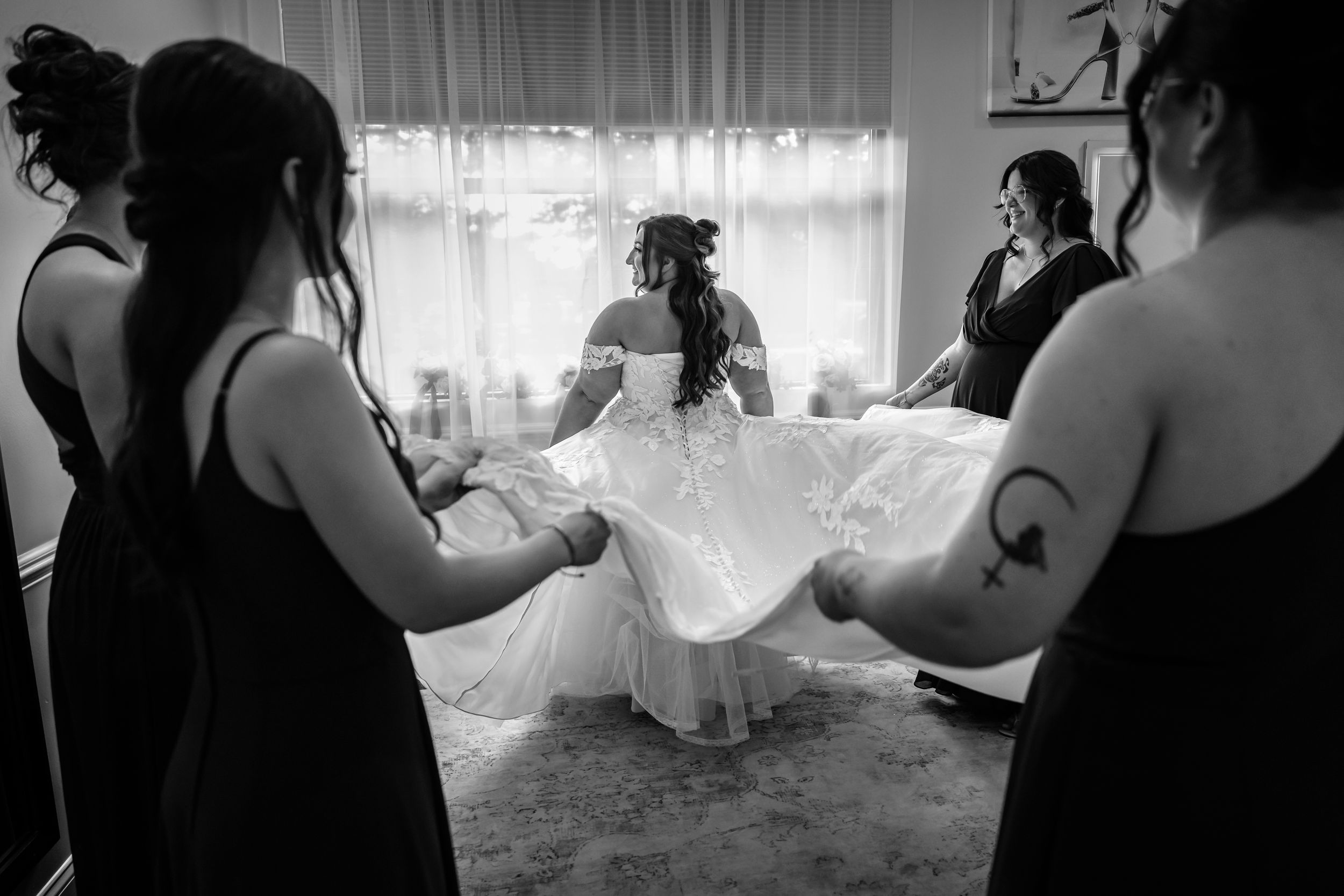 Bridesmaids helping bride with wedding dress in black and white photo.