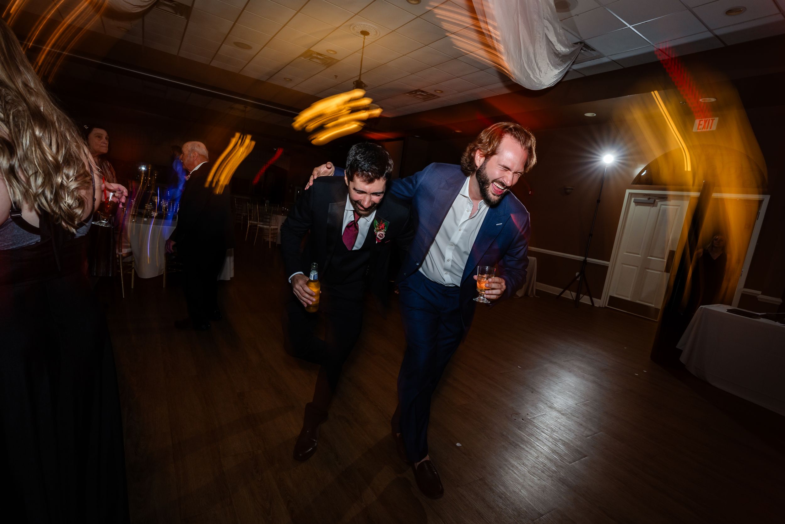 Two male wedding guests dance energetically together at a lively wedding reception celebration.