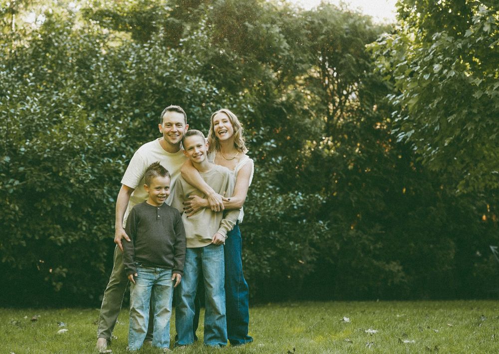 Happy family of four smiling together outdoors in a lush green park setting.