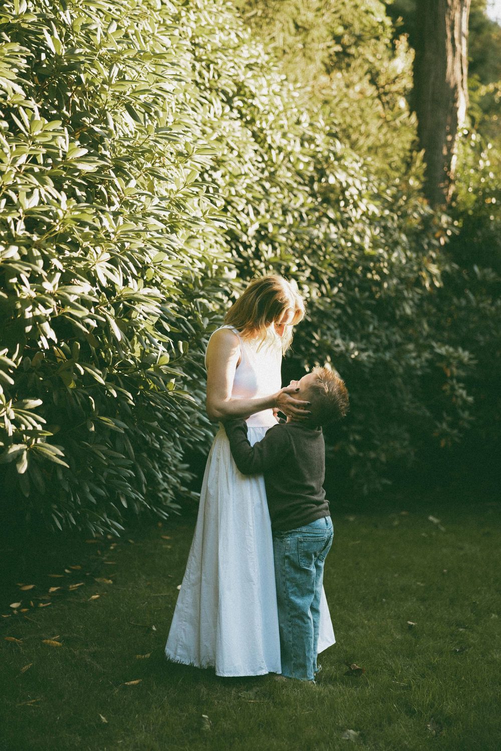 A bride in a white dress embraces a child in a lush green garden setting.