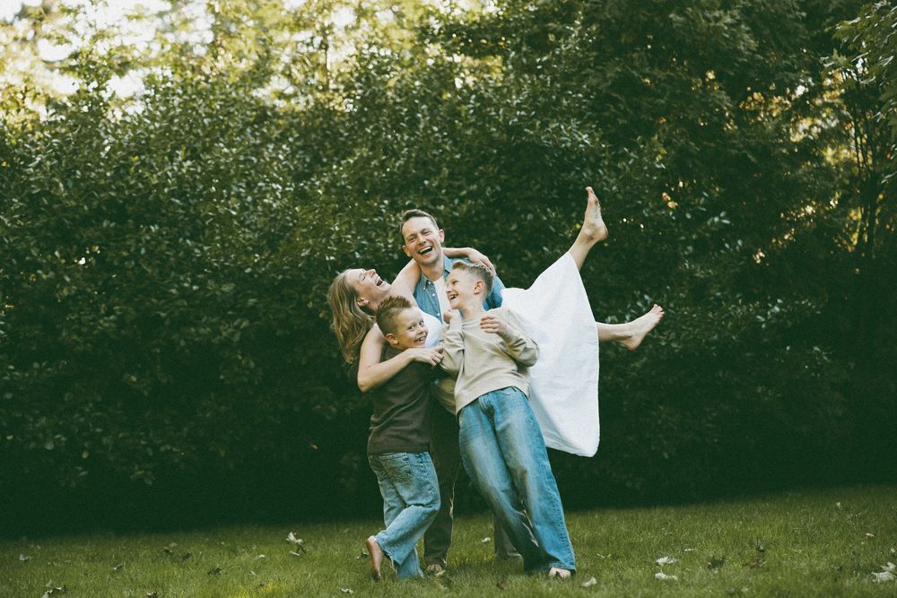 Children playing outdoors, laughing and being lifted up in a lush green garden setting.