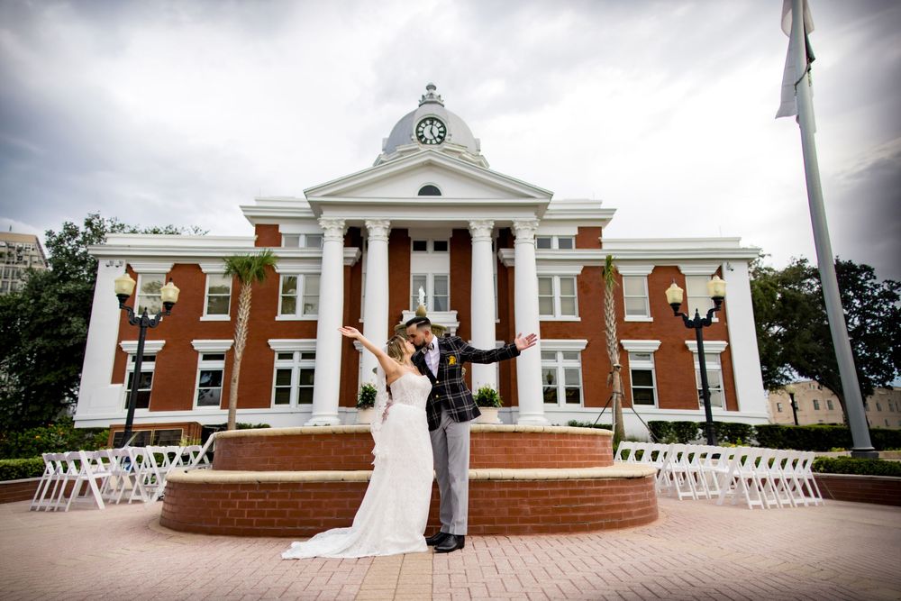 Bride and groom celebrate with arms raised outside a classic brick courthouse wedding venue.
