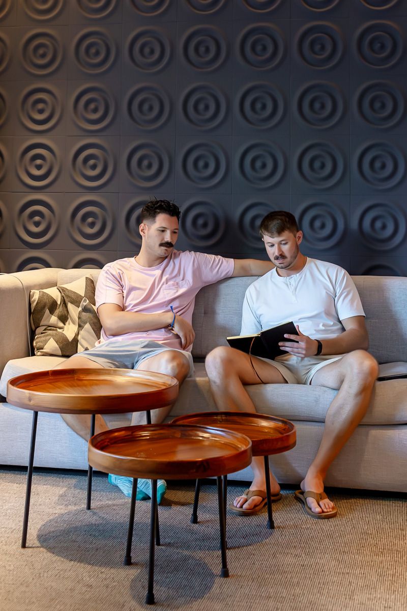 Two men sitting on a gray sofa reviewing a tablet in a modern hotel lounge with decorative circular wall panels.