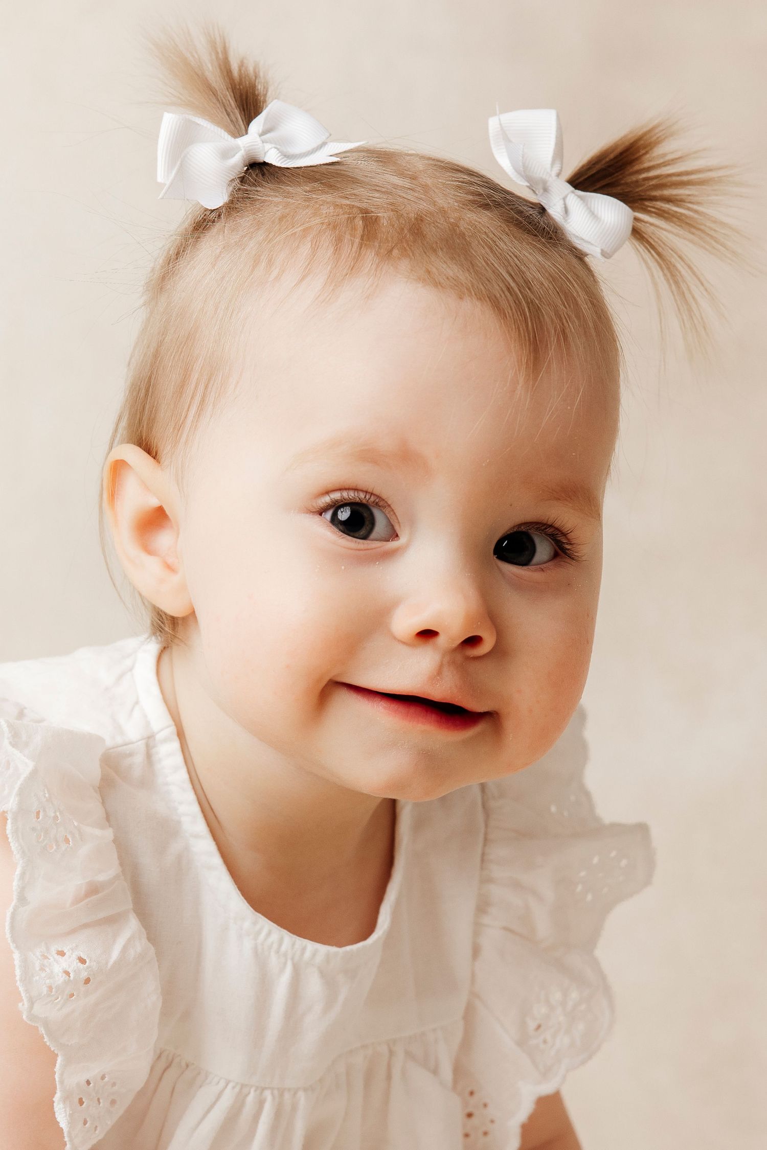 Baby girl in white dress sitting beside a number one balloon, celebrating her first birthday.