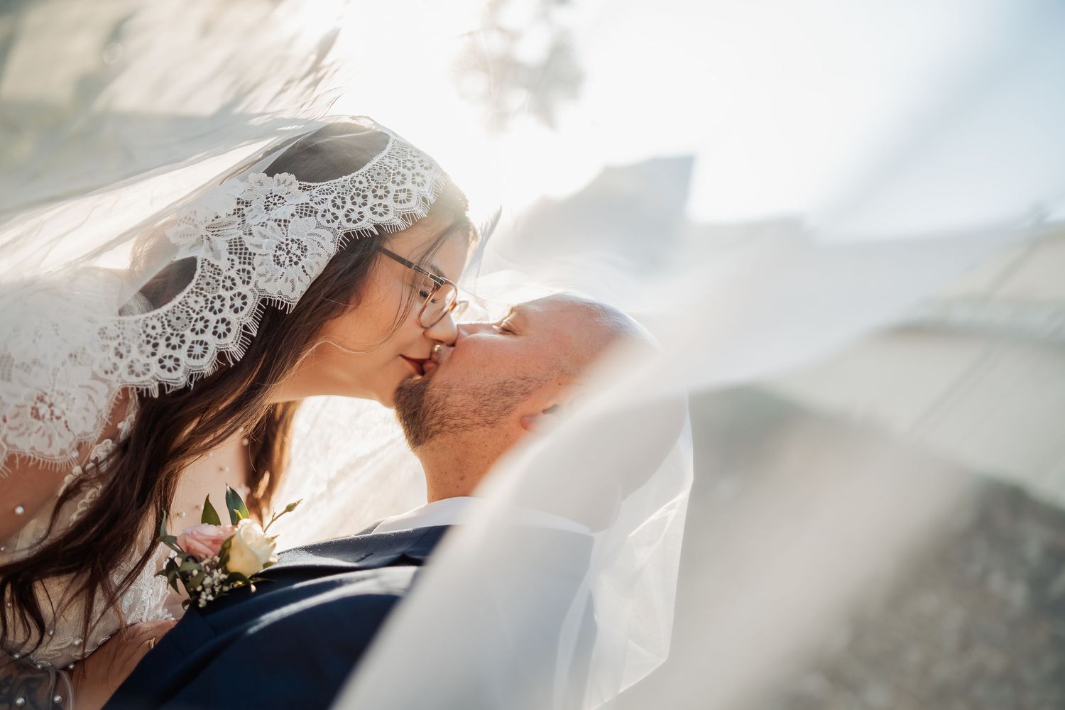 Bride and groom sharing a romantic kiss under a flowing lace veil on their wedding day.