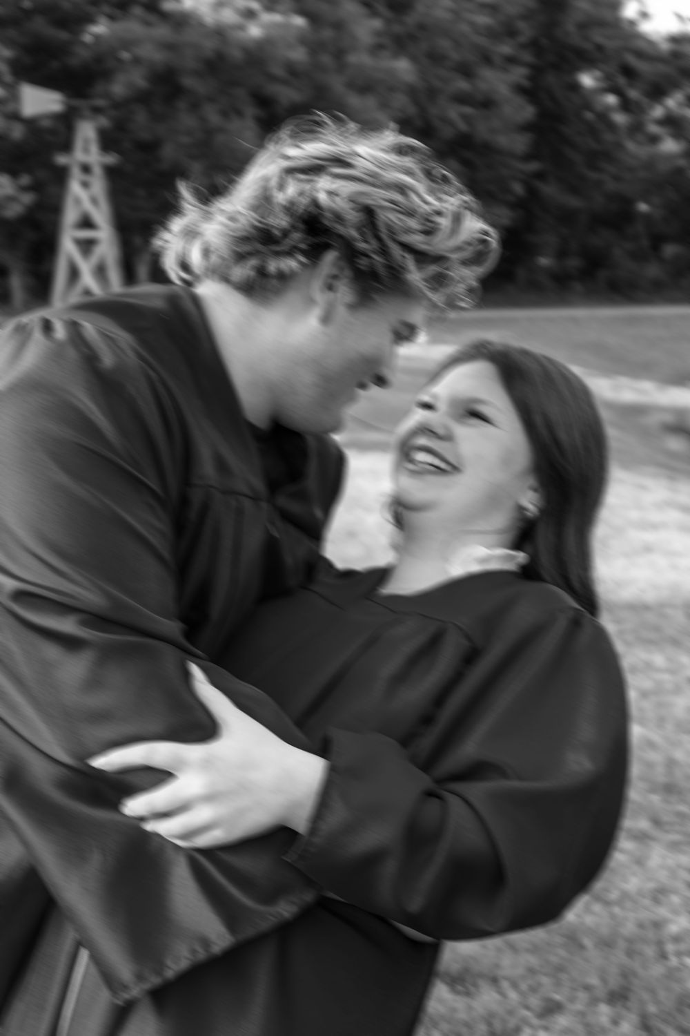 Two graduates in black gowns share a joyful embrace outdoors in this black and white photo.