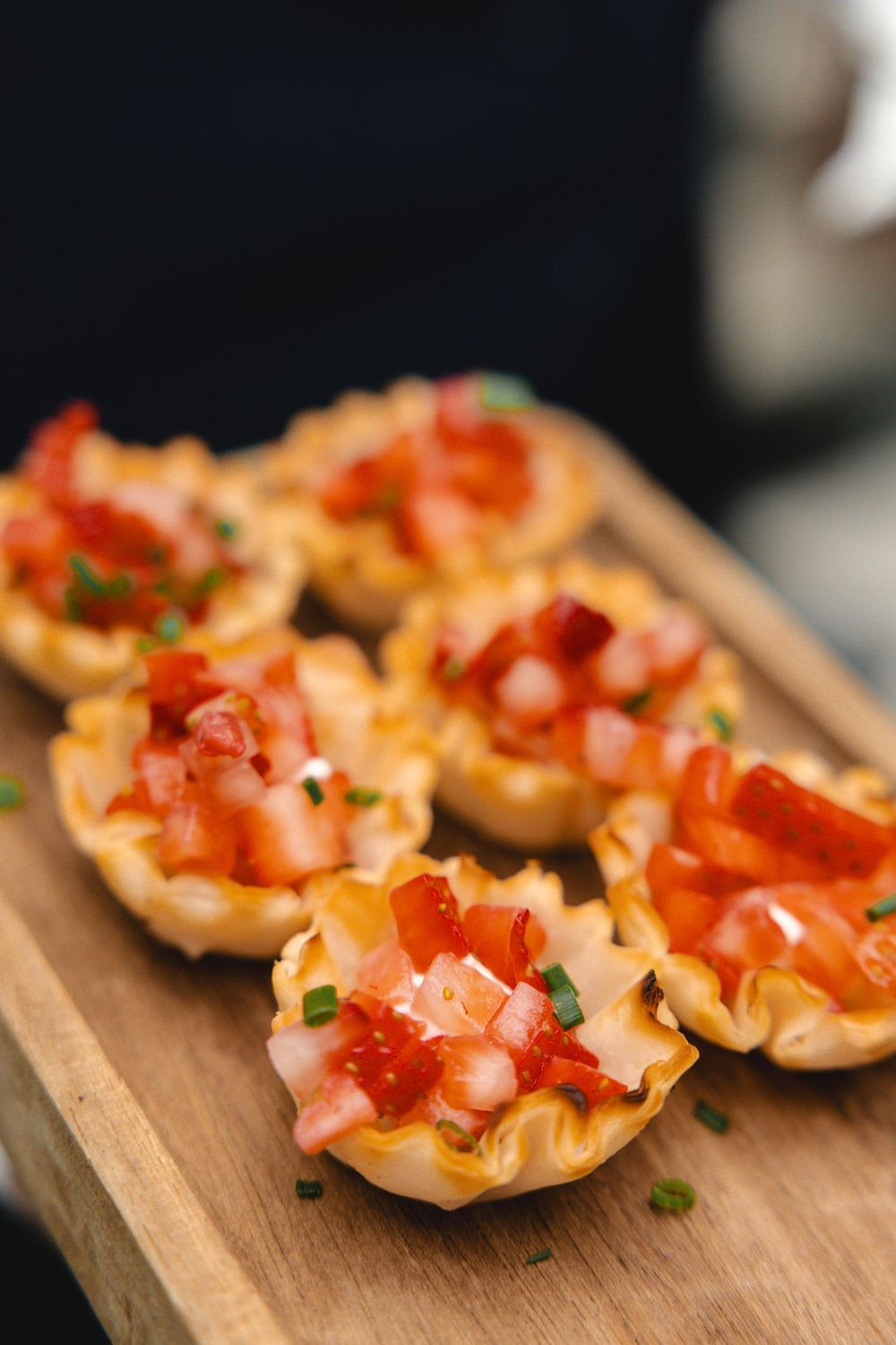 Crispy phyllo cups filled with diced fresh strawberries and chopped chives, served as elegant appetizers on a rustic wooden board.