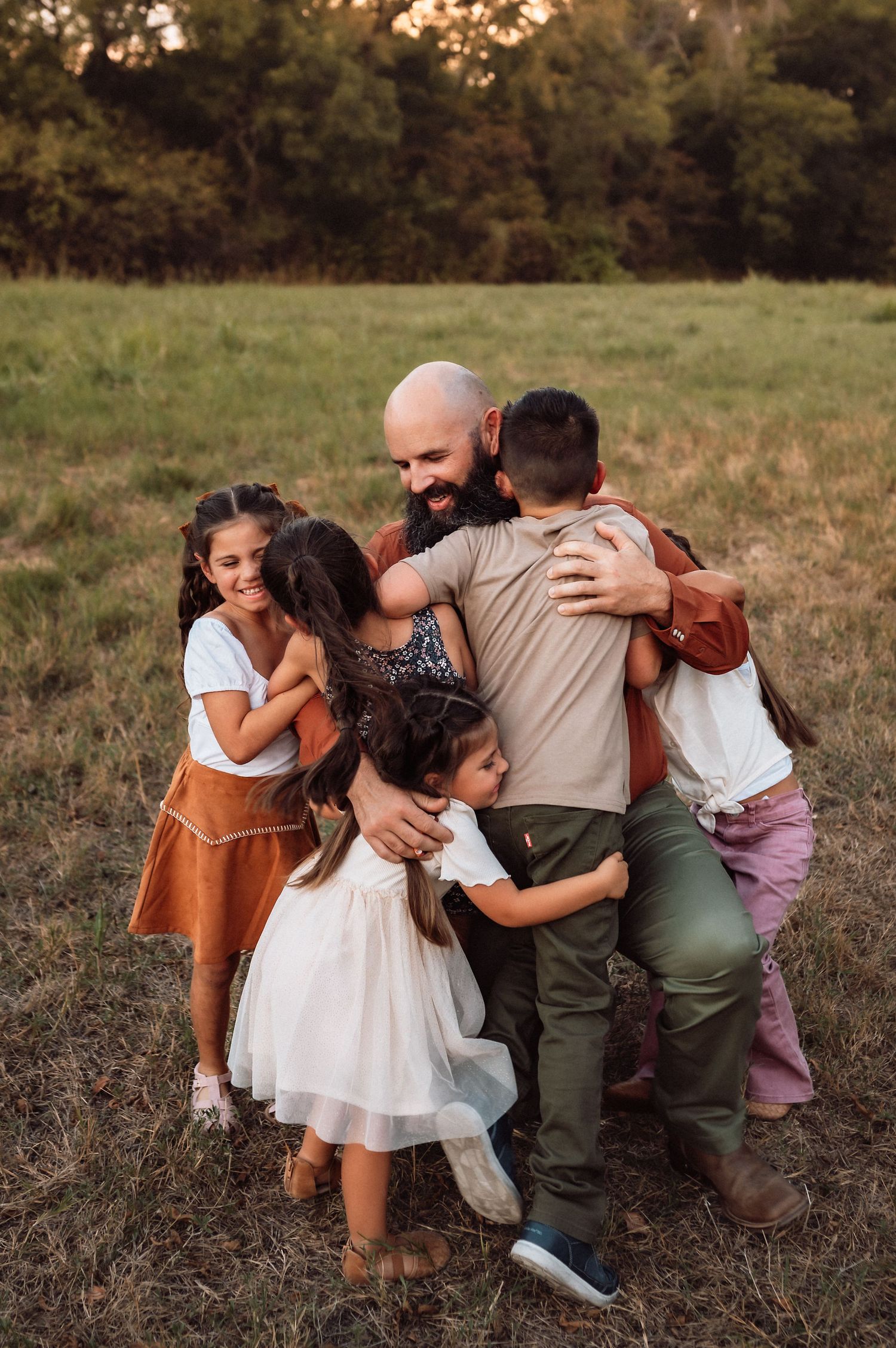Photographer with backpack captures a bearded man posing with two young children in an open grassy field at golden hour.