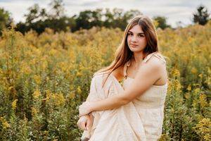 Young woman in cream dress poses gracefully among yellow wildflowers in a lush green field.