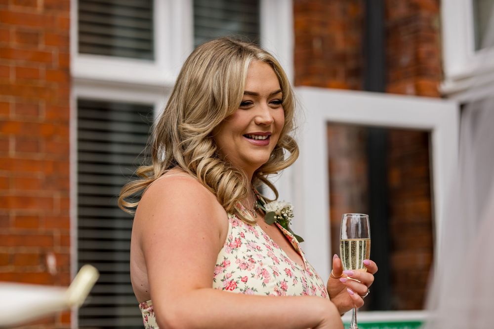 Smiling blonde woman in floral dress holding champagne glass at outdoor wedding celebration.
