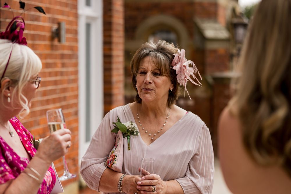 Elegant woman in pink dress with floral hair accessory holding boutonniere at outdoor wedding reception.