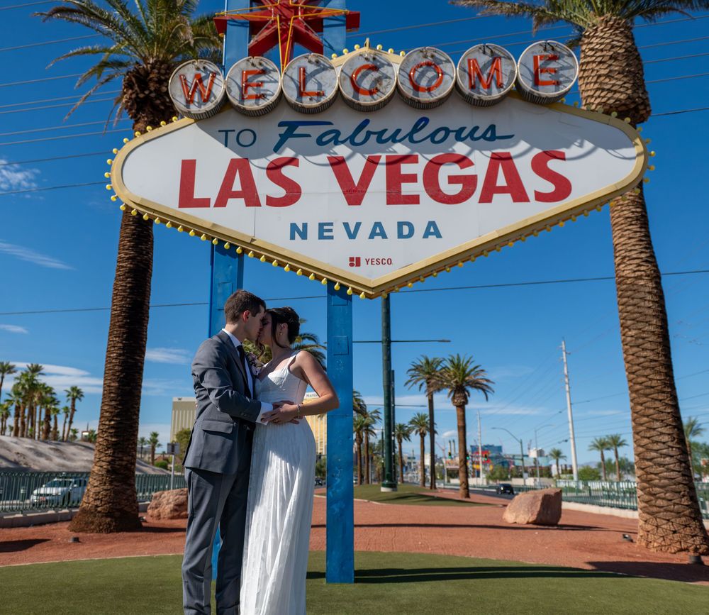 Couple sharing a romantic kiss in wedding attire beneath the iconic Welcome to Fabulous Las Vegas Nevada sign.