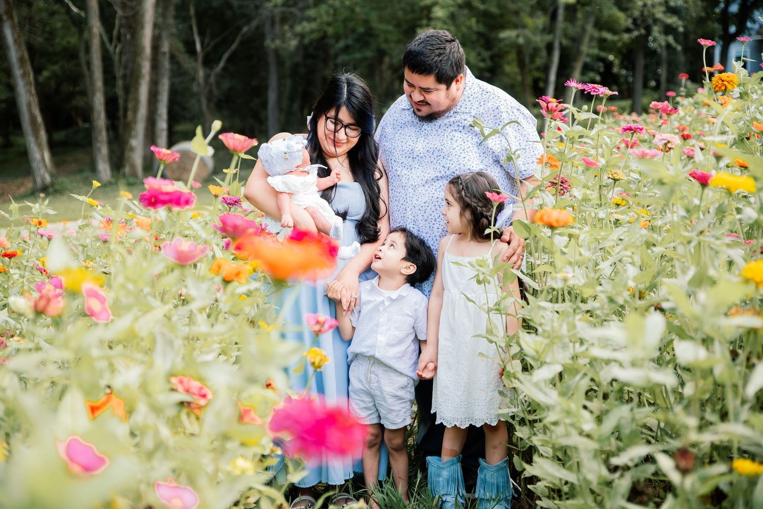 Family of five enjoying a colorful zinnia flower field, parents and children smiling together outdoors.