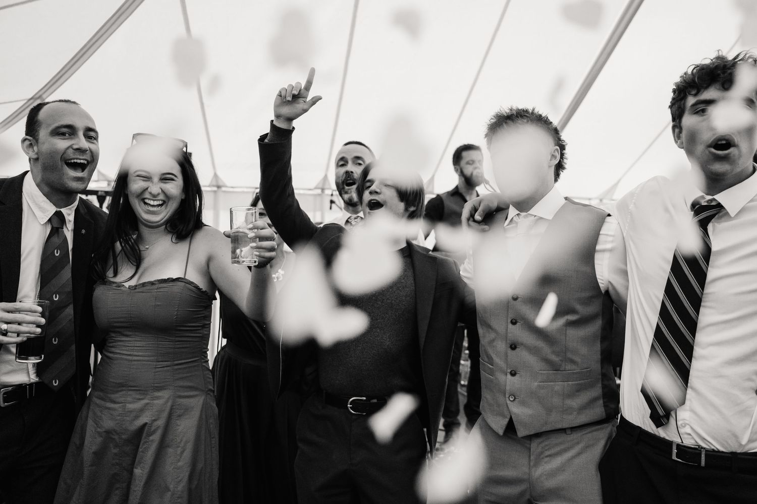 Black and white photo of joyful wedding guests celebrating with confetti flying at a festive reception party.