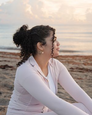 Woman in pink athletic wear sits on sandy beach at sunset, gazing peacefully at the ocean horizon.