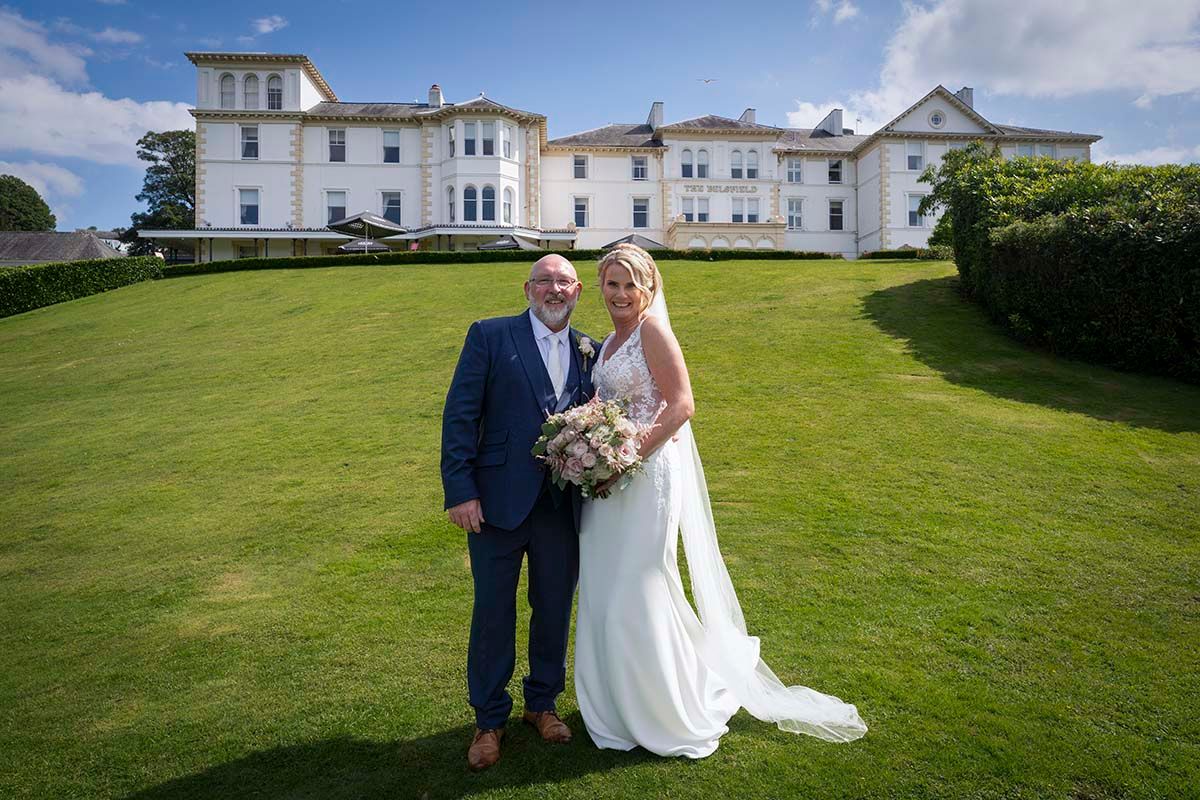 Bride and groom standing together on the lawn with the Belsfield Hotel behind them.