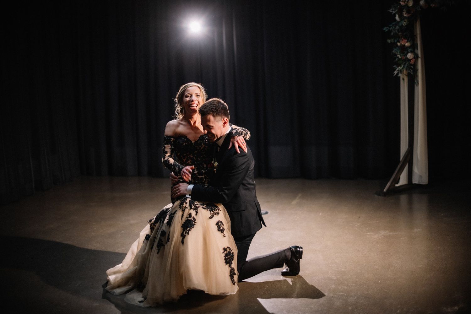 Groom down on one knee with the laughing bride in his arms at the end of their first dance