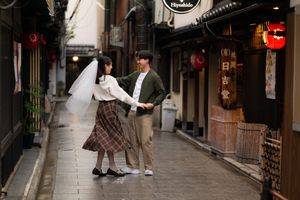 Couple in a bridal veil and plaid skirt dancing hand in hand on a quiet, lantern-lined traditional Japanese street.
